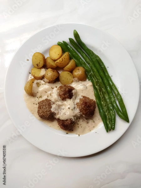 Fototapeta Meatballs smothered in creamy mushroom sauce with potatoes and green beans isolated on a white background. Perfect for a comforting meal.