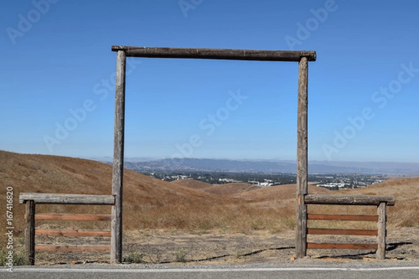 Fototapeta Old Wooden Framed Entrance to Farmland, with a blue sky and mountain range in the distance