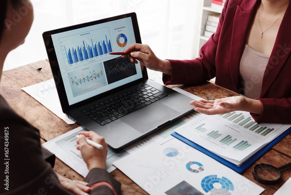 Fototapeta Businesswomen analyzing financial charts and graphs on laptop during meeting