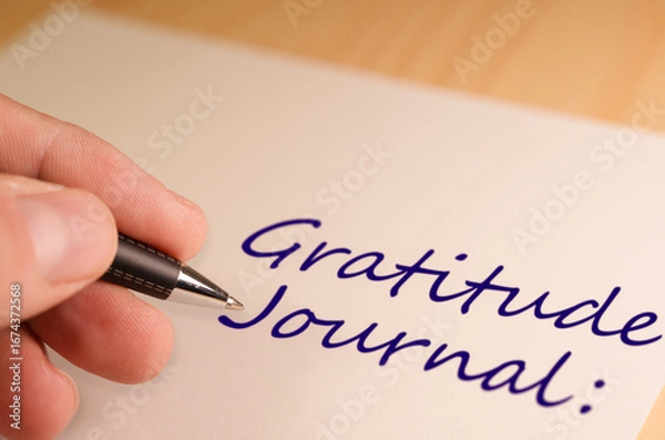 Fototapeta Hand writing the words gratitude journal on a notebook with a pen, promoting mindfulness and self care