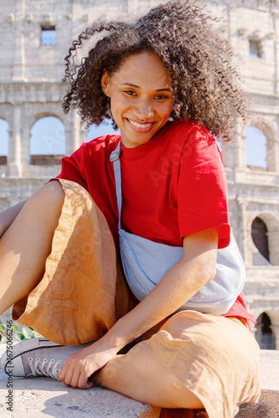 Fototapeta A joyful young woman poses with a big smile in front of the iconic Colosseum, showcasing a beautiful blend of casual style and the historical beauty that defines Romes vibrant culture