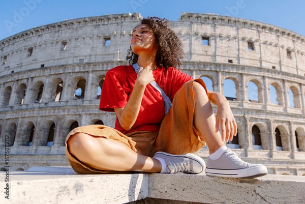 Fototapeta A joyful traveler stands proudly in front of the iconic Colosseum, capturing a moment that beautifully showcases a delightful blend of ancient history, stunning architecture, and modern style