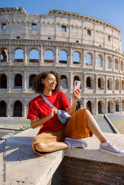 Fototapeta A cheerful young woman enthusiastically takes a vibrant selfie at the iconic Colosseum in Rome, fully enjoying her delightful travel experience while making beautiful memories along the way