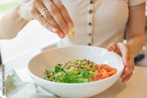 Fototapeta Close-up of a woman adding lemon juice to a green salad with salmon.