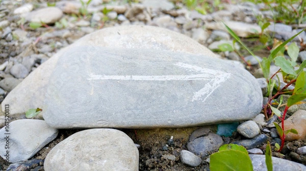 Fototapeta Painted arrow on stone show direction on dry rocks close to river side close up