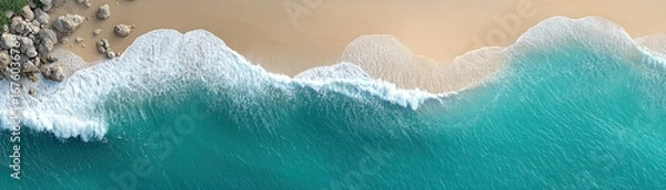 Obraz Aerial view of turquoise waves crashing onto a sandy beach with rocks on the shore.