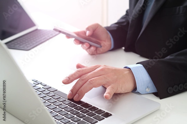 Fototapeta Businessman using laptop and smartphone at office desk