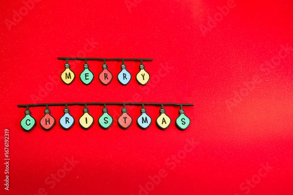 Obraz Christmas garland made of colored light bulbs spelling out “Merry Christmas” on a red background. Wooden letters. Space for text