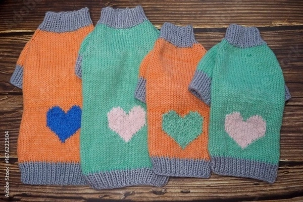 Fototapeta top view of four knitted orange and mint dog sweaters with hearts and gray elastic of different sizes on wooden background. warm pet clothes. cozy