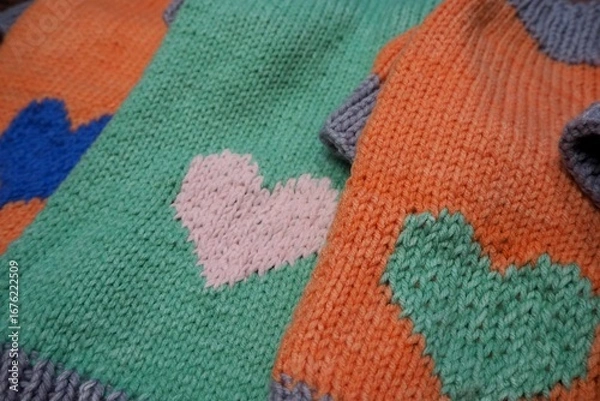 Fototapeta side view of knitted orange and mint dog sweaters with hearts and gray elastic of different sizes on wooden background . warm pet clothes . cozy