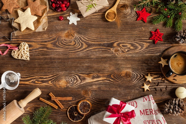 Fototapeta Christmas baking in the form of stars and other decorations: gift with red ribbon, branch of fir tree, cones, cookies, cinnamon, berries, snowflakes. View from above. Copy space