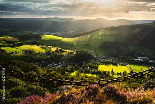Fototapeta The Sauerland landscape seen from Bruchhauser Steine ​​in Olsberg, Germany, at sunset. Beautifully lit fields and mountains with wind turbines in the background.