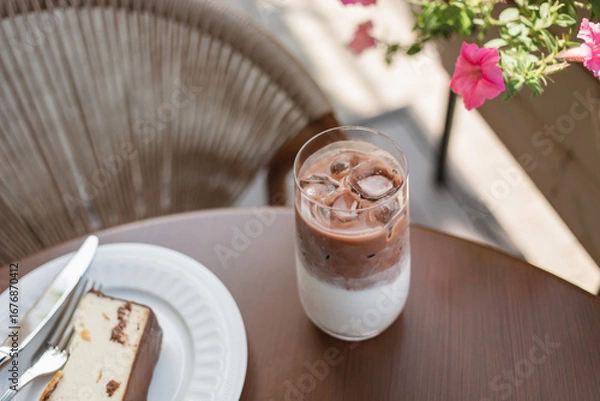 Fototapeta Close-up of an iced cacao drink and a slice of cake on a table at a street cafe in summer.
