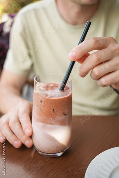 Fototapeta Close-up of a man sitting at table on summer terrace and enjoying refreshing iced latte coffee. 