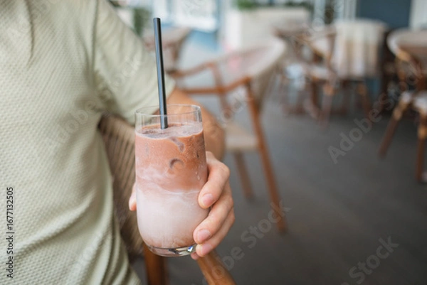Fototapeta Close-up of a man sitting at table on summer terrace and enjoying refreshing iced latte coffee. 