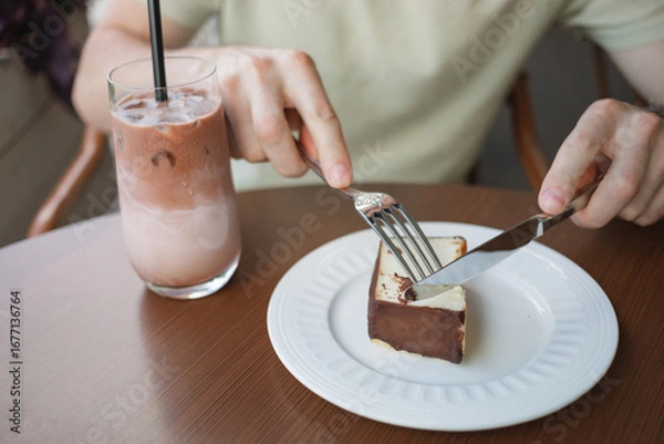 Fototapeta Close-up of a man enjoying a slice of cheesecake and a glass of iced latte coffee, while sitting on the terrace of a cafe.