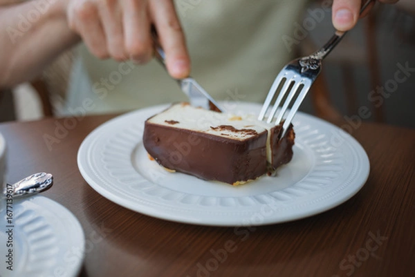 Fototapeta Close-up of a man cutting a slice of cake while sitting on a terrace at a cafe.