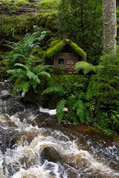 Obraz The image shows a small waterfall scene near the ruins of the Ieriķi Mill, where a stream flows through a lush green forest.