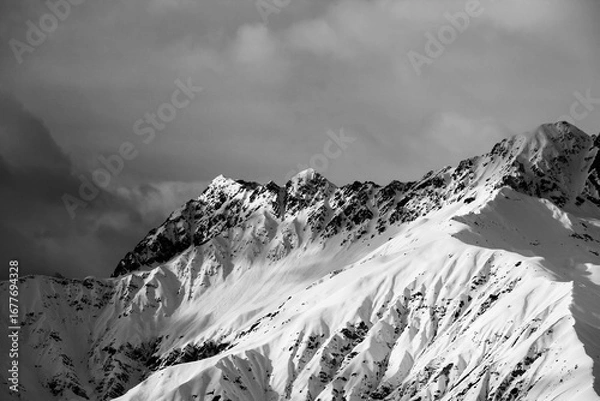 Fototapeta Black and white high snowy sunlight mountain and cloudy grey sky at winter evening