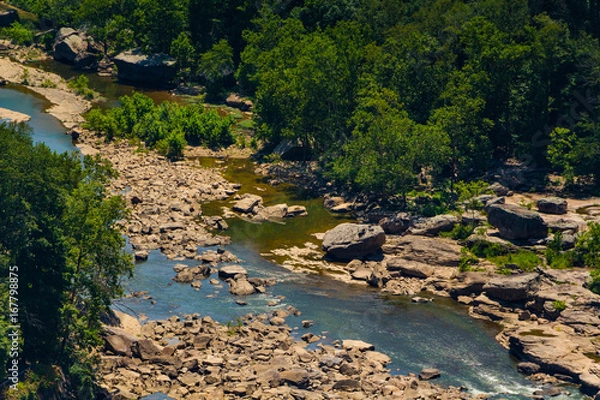 Fototapeta A rocky waterway visible from Hawks Nest State Park in southern West Virginia, with green trees surrounding it, and a few large stones nearby.
