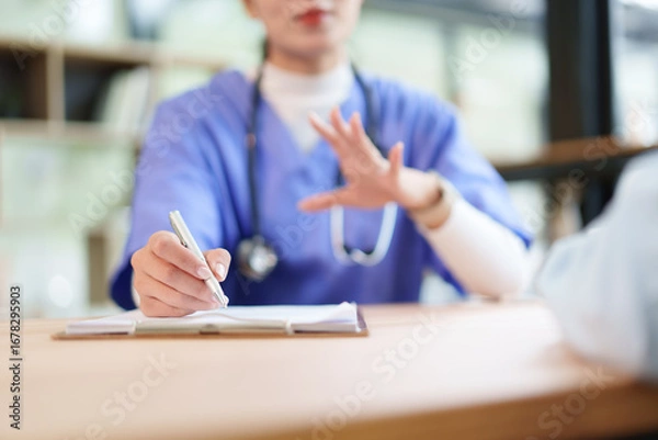 Fototapeta Nurse writing patient notes on clipboard while consulting with patient, focused medical documentation and compassionate communication