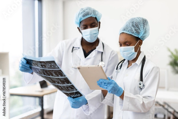 Fototapeta Two adult medical professionals discussing diagnostics, one viewing scans and one holding clipboard, collaborative environment