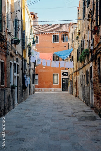 Fototapeta Typical Venetian view with narrow street, colorful ancient buildings and laundry hanging to dry.
