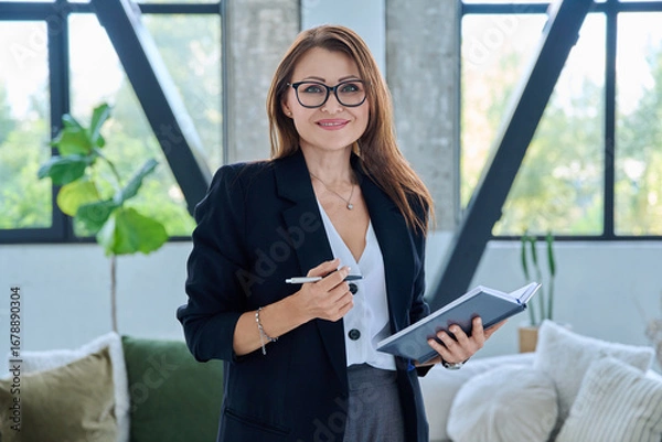 Fototapeta Portrait of smiling middle-aged confident business woman with notebook