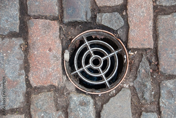 Fototapeta A arial view of a drain cover inbatween a bricked path