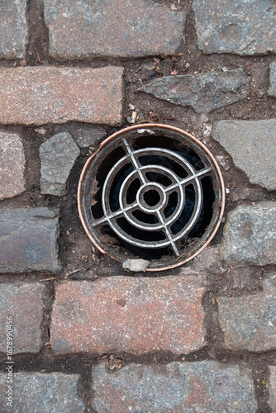 Fototapeta A arial view of a drain cover inbatween a bricked path