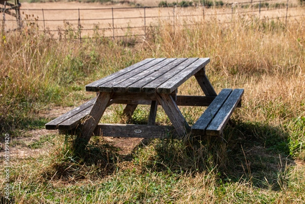 Fototapeta A view of a wooden bench in the middle oif a grass field