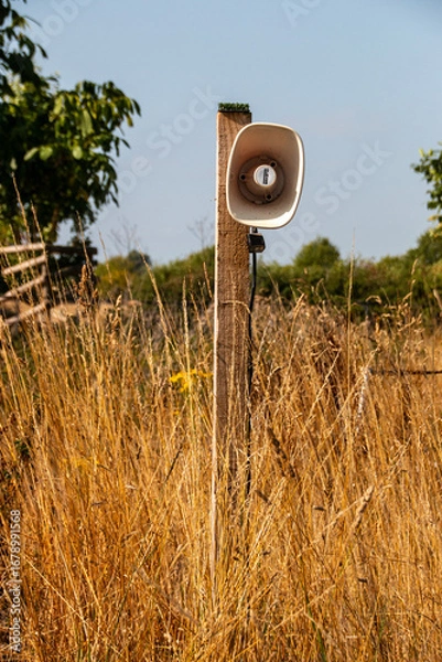 Fototapeta A view of a speaker on a pole in a open grass public area