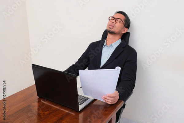 Fototapeta A businessman at his working desk showing stressed expression