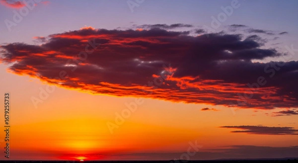 Fototapeta A vibrant sunset paints the sky with fiery hues, casting a warm glow over the horizon.