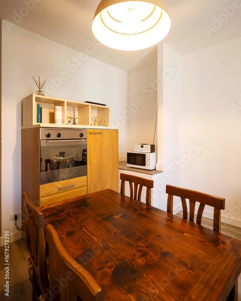 Fototapeta Interior of a kitchen with lots of wood in an old Italian style. In the foreground is the table and chairs.