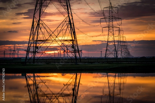 Fototapeta Electricity pylons disappear over horizon on marshland at sunset