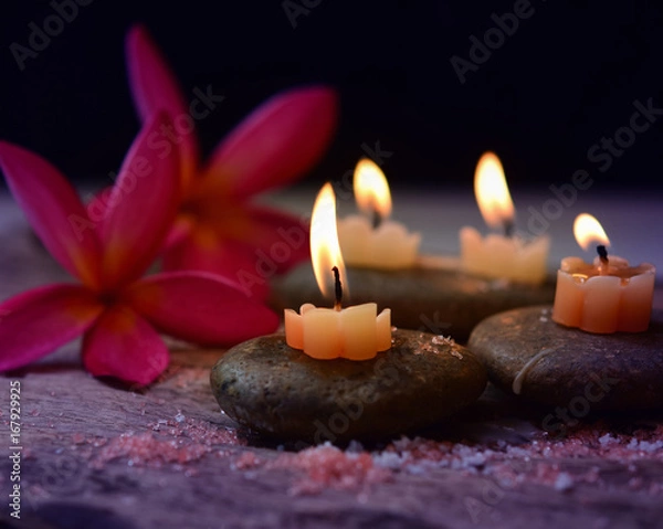 Obraz Soft Light and candles scented with refreshing fragrance and salt scrub on black stones, including plumeria flower, spa concept, Thai massage on black background.