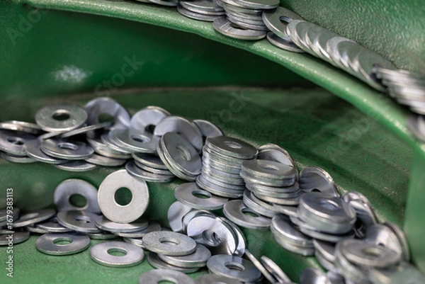 Fototapeta Steel Washers on Vibratory Feeder Track in Industrial Setting. Close-up shot of flat metal washers being oriented on a green vibratory feeder for use in automated assembly. Selected focus