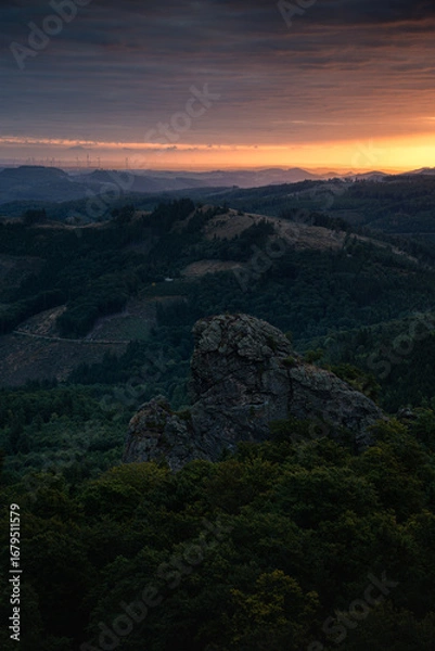 Fototapeta A landscape of the Sauerland region in Germany, with the Bruchhausen Steine ​​rocks in the foreground. In the background, hills illuminated by the rising sun. Vertical view