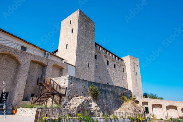 Fototapeta Rocca Albornoziana, an imposing medieval fortress, rises against a vibrant blue sky, highlighting its historic architecture and offering panoramic views of Spoleto, Italy