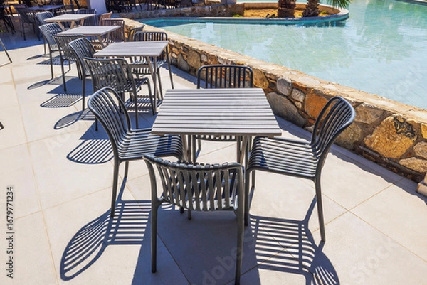 Fototapeta Close up view of outdoor restaurant terrace with black chairs and tables beside pool in sunny resort background. Kos. Greece.