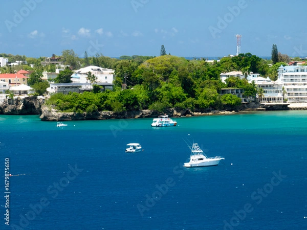 Obraz A long, sandy beach stretching along the coast, lined with lush green forest and resort-like buildings further away. A wide, stunning bay with vibrant blue and turquoise water, where several boats are