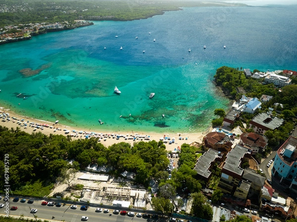 Obraz A long, sandy beach stretching along the coast, lined with lush green forest and resort-like buildings further away. A wide, stunning bay with vibrant blue and turquoise water, where several boats are