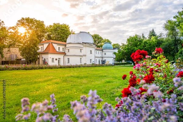 Fototapeta Sunlight cascades over Stefanik Observatory on Petrin hill, surrounded by colorful flowers. The scene captures the beauty of Czech astronomy amidst nature's tranquility.