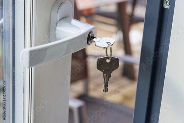 Fototapeta Terrace door ajar with key in lock and outdoor tables beyond