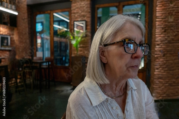 Obraz Senior Woman Sitting in a Cozy Cafe Wearing Glasses and Reflecting