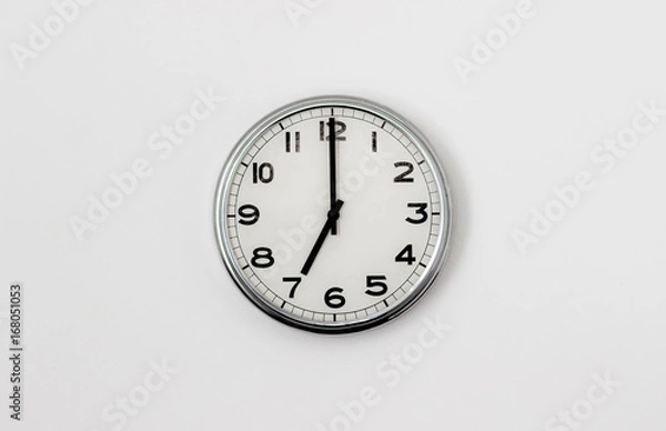 Fototapeta White Clock hanging on a white wall showing time 7:00