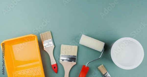 Fototapeta Scattered paint tools with roller, brushes, tray and bucket on green background for interior renovation and DIY project concept