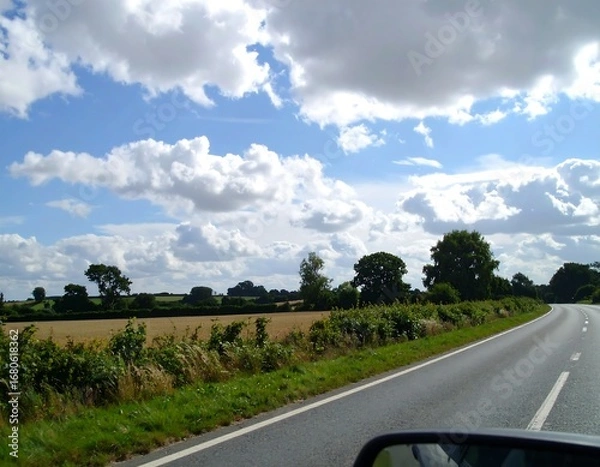 Fototapeta Country road scene with fluffy clouds and green fields