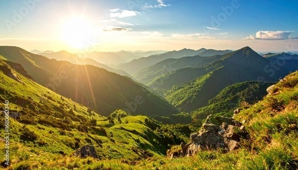 Fototapeta Sun setting over mountains with a clear view of green valley from the mountain top